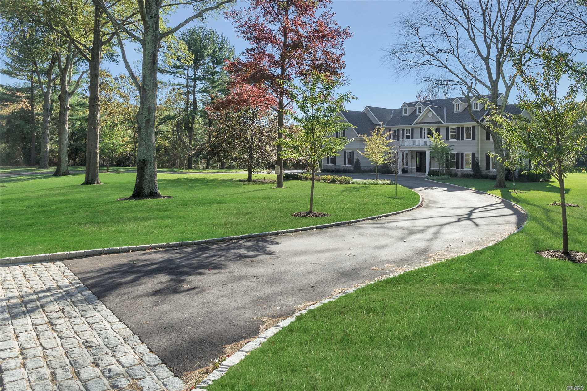 Imagine living in a brand new, state-of-the-art six-bedroom, five-and-a-half-bath home with a traditional manor-house style in a beautiful mature neighborhood of two-acre-plus homes and with only a modicum of passersby. Such is what this magnificent home offers. Standing majestically on 2.11-acres of sweeping emerald lawns dotted by towering mature trees and enfolded on three sides by walls of foliage, and approached by a long circular drive, this fabulous, newly finished Colonial has it all, including room for a possible pool and tennis court and an ideal location. Situated in the heart of Old Westbury, the home part of a section of homes that has one entrance, two cul-de-sacs, and a circular road - ideal for pleasant strolls or biking. Practically surrounded by golf courses and universities, the area is also within easy reach of major expressways for easy commuting. Long a popular area for Manhattan’s magnates and luminaries, Old Westbury is just 30 minutes by railway or highway from Manhattan and Kennedy and LaGuardia airports. Conveniently located near parks and museums, it is just a short drive from fine dining, premier shopping, miles of public equestrian trails, polo club, yacht clubs and beaches.  
Its traditional center-hall floor plan has been beautifully tweaked to allow easy, open flow throughout its entertaining spaces, with French doors ready to close for privacy when needed. Boasting gleaming hardwood floors, elegant crown moldings, and a myriad of windows and French doors, the first floor welcomes guests through a vestibule, with guest closets, into a spectacular two-story entrance foyer with graceful bridal staircase and stunning powder room. To the left, is the banquet-sized formal dining room in all its elegance, and to the right, a parlor is open to the inviting great room with its magnificent marble-faced gas fireplace and windows plus French doors opening to the rear property. Entered from the parlor and the living room, the spacious and sunny library/den is flooded with verdant views through many windows on three exposures.
Entered from the great room and the foyer, spacious sun-drenched eat-in-kitchen offers the finest in today’s finishes and appliances. Gray glass-tile backsplash accents custom oak stained walnut cabinetry with white quartzite countertops and farm sink while a large cherry center island, with prep sink and seating area, coordinates with the hardwood floors. High-send appliances include a 6-burner stainless-steel gas stove with griddle and double-oven; a side-by-side, integrated full-size refrigerator and full-size freezer; plus an integrated dishwasher; and a stainless-steel built-in microwave. A butler’s pantry, accessing the dining room, provides cabinetry, similar to the kitchen, plus entry to a large walk-in pantry. Fully open to the kitchen and the great room, the sunny breakfast area overlooks the rear property through a wall of French windows and door to the patio – idea for al fresco dining. A hall off the kitchen, with back stairs, leads to the attached three-car garage, a large mudroom with many closets, including one walk-in, and a well-equipped laundry room. A nearby guest suite features a designer bath with shower and a sunny bedroom with double-closet.
On the second floor, the palatial master suite enjoys its own private wing including an immense master bedroom with romantic gas fireplace; a dressing room with dressing table and pocket doors opening to two spacious walk-in closets; and a luxurious white-marble master bath. Several windows above a free-standing soaking tub allow sunlight to dance across the custom twin vanity, huge frameless-glass-enclosed shower, and door to the water closet. Across the foyer, the remainder of this level includes four additional bedrooms, each with walk-in closets, two with baths en suite, and two sharing a hall bath next to a spacious upstairs lounge. The full unfinished basement provides many opportunities for storage and expansion. Come experience the serenity and splendor of this exceptional, brand-new property, a perfect setting for today’s gracious North Shore lifestyle.